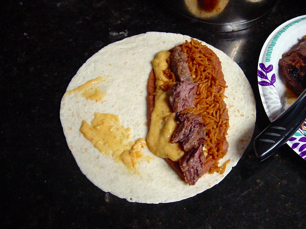 Cheese sauce on a burrito with steak, beans, 
 and rice.