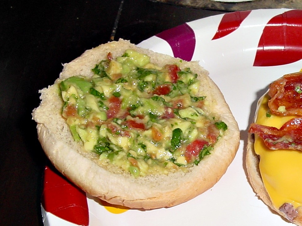 Visible chunks of avocado, tomato, and cilantro
 resting in the top of a hamburger bun.