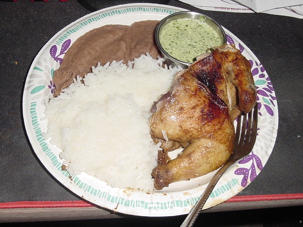 Half of a roasted hen, served with green sauce,
 white rice, and refried beans.