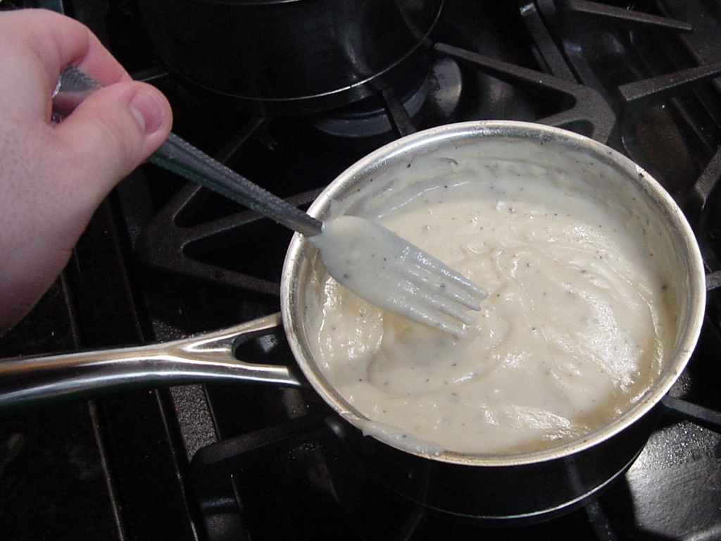 Thick gravy in a saucepan, sticking to a fork
 being pulled out of the mixture.